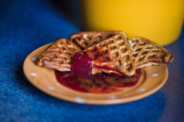 Macro shot of just cooked, delicious, tasty and hot yogurt pancakes with strawberry sauce on yellow and white plates in kitchen, next to stove. Dinner is ready. Sweet golden brown waffles with jam