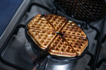 Just cooked, delicious, tasty, hot yogurt pancakes on waffle iron on fire stove in kitchen. Dinner is ready. Sweet golden brown waffles ready to be eaten
