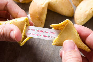 Hand opening fortune cookie with message on paper on wooden table - obrazy, fototapety, plakaty