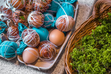 Easter eggs prepared for dyeing in onions peels, decorated with natural fresh leaves, plants, rice, colorful fabric and tied with white threads. Eggs laying in wicker wooden basket full of green grass - obrazy, fototapety, plakaty