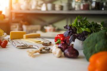 Cheese with fresh vegetables basil and cutting board on white, shabby, rustic kitchen table. Ingredients for cooking on the vintage rural kitchen. Healthy traditional food. Selective focus. Free space