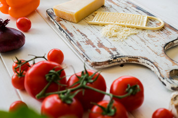 Cooking fresh vegetarian lunch from tomatoes, chees, greenery and onion. Vegetables prepared for making meal. Wooden rural table and ingredients on light background. Vegetarian food, cooking concept.
