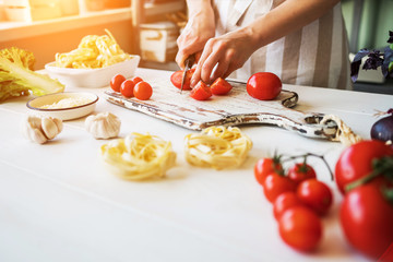 Close up of unrecognizable cook,cutting tomatoes and other vegetables with knife while working in home kitchen. Woman cooking salad, bio food preparing. Vegetarian food, health lifestyle concept.