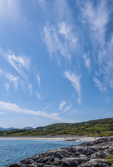 View of a beautiful sandy beach from the rocks on a sunny day with clear blue ocean and blue skies. Taken in summer in Renvylle, along the Wild Atlantic Way, Ireland.