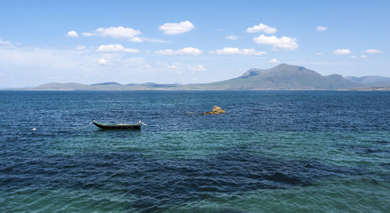 One fishing boat on calm, turquoise water on a sunny summer day with mountains in the distance. Taken along the Wild Atlantic Way in Ireland.