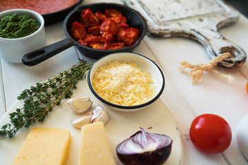 Italian food cooking ingredients on white table with sun-dried tomatoes, herbs and garlic, fresh vegetables, pasta, cheese parmesan and spices. Balanced nutrition. Cooking, culinary, food concept.