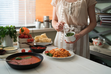 Woman making homemade pasta with tomato sous and cheese over old wooden table. Tomato, olive oil, spices, herbs, cheese, tomato sauce on a weathered wooden table in the summer sun's rays. Organic food