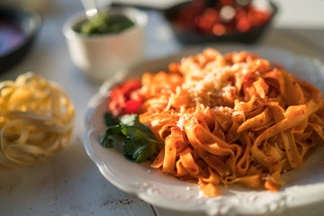 Pasta with spicy tomato sauce, parmesan and basil. Plate with delicious pasta, cheese, pan with organic tomato sauce and kitchen board on wooden table, top view. Products for cooking. Soft focus.