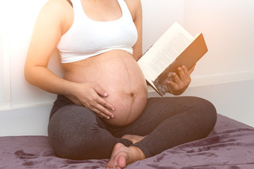 close up of pregnant woman reading book and relax time in the morning and sitting on bed at home bedroom