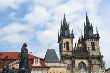 Obraz premium A statue looks onto the Our Lady of Tyn Church, Prague. The sky is blue, with white clouds.