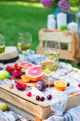 Picnic background with white wine and summer fruits on green grass, summertime party