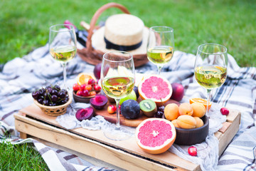 Picnic background with white wine and summer fruits on green grass, summertime party