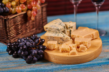 Closeup image of delicateness Danablu pieces lying on board next to fresh juicy grape clusters.Fruit and moldy cheese in peasant style.