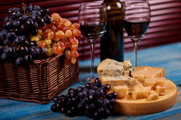 Couple glasses of dry chardonnay standing on table for enjoyable dinner with moldy delicious pieces of cheese and basket with natural fruit.