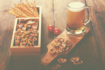 Tasteful light beer in glass with bubbles and foam for degustation in rustic style.Salty straw, crispy mini pretzels, crackers in box.