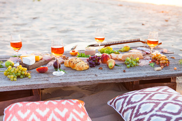 Picnic on beach at sunset in boho style. Romantic dinner, friends party, summertime, food and drink concept