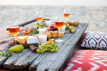 Picnic on beach at sunset in boho style. Romantic dinner, friends party, summertime, food and drink concept