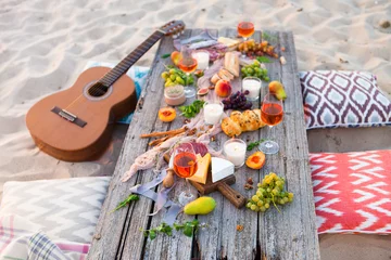 Photo sur Plexiglas Pique-nique Picnic on beach at sunset in boho style. Romantic dinner, friends party, summertime, food and drink concept