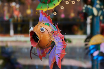Fototapeta na wymiar Colorful souvenir background. Hanging decoration in the market. Handmade metallic fish hanging on the tourist market. Sale of souvenirs. Funny handmade fishes with bright colorful patterned.