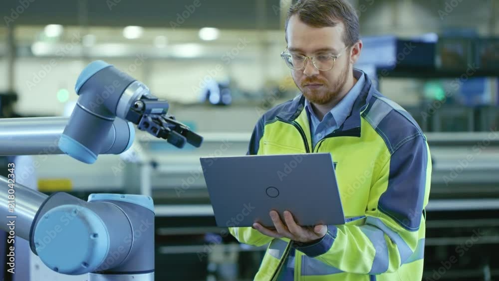 Poster At the Factory: Automation Engineer Uses Laptop for Programming Robotic Arm. New Era in Automatic Manufacturing Industry.