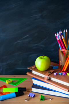 Back to School cocept. Still life with school books, pencils and apple against blackboard background