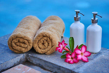 Obraz na płótnie Canvas Plumeria flowers, spa cosmetic and towels over blue water background, spa still life, travel and tourism, conceptual photo of a summer vacation.