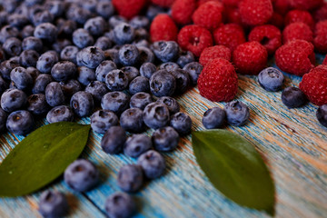 Berries on blue  background. Summer or spring organic berry.  Agriculture, gardening, harvest concept. Fresh sweet blueberry, raspberry fruit. Healthy food. Selective focus. Top view with copy space.