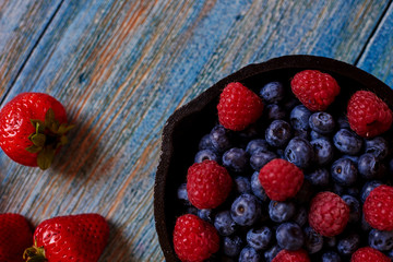 Raspberry, strawberry and blueberry closeup on blue wooden table.