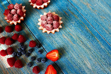 Delicious mini tarts made of oatmeal with fresh raspberries and custard on a wooden blue table. A homemade dessert made from delicious mini cakes. Healthy snack. Useful breakfast. Selective focus.