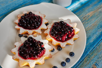On a large white plate cook laid out freshly cooked tartlets with dzheomo Svezhnev of blueberries, currants and blueberries
