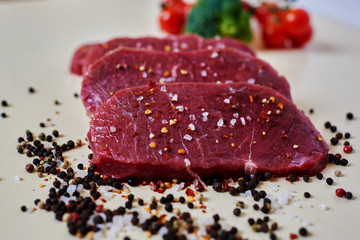 Close-up on a white kitchen table, the housewife sliced pork tenderloin, seasoned meat fragrant herbs