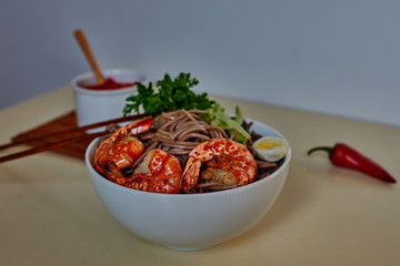 Traditional Japanese food. Noodles with prawns on the kitchen table. Seafood. Buckwheat stir-fry noodles with seafood - shrimps,  in asian bowl with cooking chopstick. Healthy food. Selective focus..