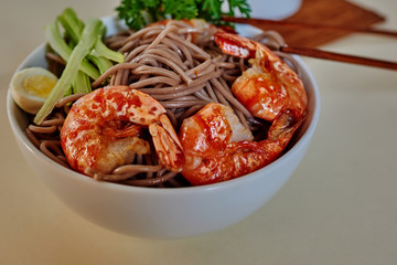 Traditional Japanese food. Noodles with prawns on the kitchen table. Seafood. Buckwheat stir-fry noodles with seafood - shrimps,  in asian bowl with cooking chopstick. Healthy food. Selective focus..