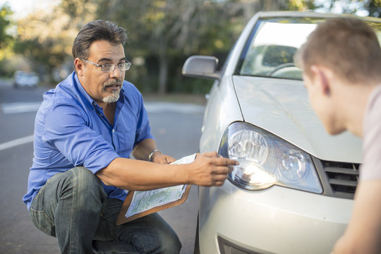 Learner driver with instructor checking headlight of a car