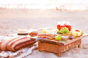 Foto auf Acrylglas Picknick Picknick am Strand bei Sonnenuntergang im Boho-Stil. Konzept im Freien abends gesundes Abendessen mit Obst und Saft