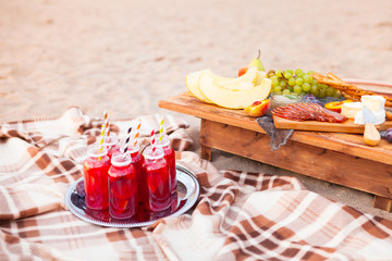 Picnic on the beach at sunset in the style of boho. Concept outdoors evening healthy dinnner with fruit and juice
