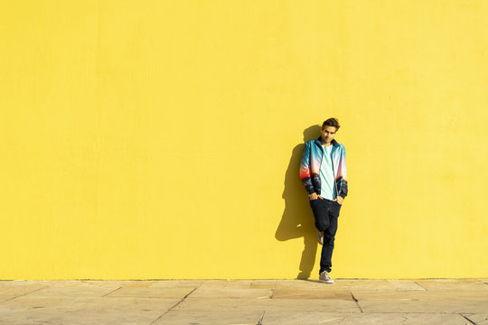 Man leaning against yellow wall with hands in pockets