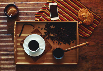 Top view on the table is a wooden dressing with a cup of coffee on a saucer near pots with about brewed coffee, biscuits lying beside a little broken off