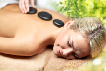 Obraz premium beauty, wellness and relaxation concept - close up of beautiful young woman having hot stone massage in spa over green natural background