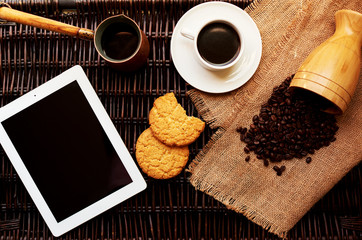 On a dark wicker rattan table, a light breakfast is served the plate, a cup of fresh coffee and a round oatmeal cookies