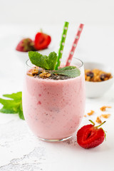 Pink strawberries, banana smoothie with granola and chia seeds in glass on light white concrete background. Top view. Copy space.