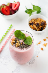 Pink strawberries, banana smoothie with granola and chia seeds in glass on light white concrete background. Top view. Copy space.