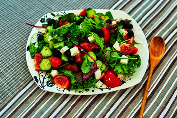 Bright fresh summer salad with cherry tomatoes, arugula, and a mix of various herbs, feta cheese is cut into small pieces, the salad served on big white plate