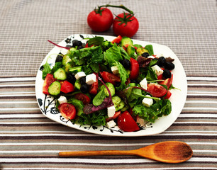 Bright fresh summer salad with cherry tomatoes, arugula, and a mix of various herbs, feta cheese is cut into small pieces, the salad served on big white plate