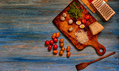 Food background with copy space. Tomatoes cherry, parmesan cheese, quail eggs and salad on old village table. Italian country kitchen with old  utensils. Rustic style. Top view. Selective focus