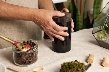 Women's hands grinding coffee beans in black coffee-grinder. Close up.