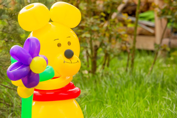 Yellow bear with flowers from balloons congratulates with a holiday in the garden on a background of spring evil