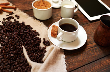 On the table in the office in a white cup of fresh black coffee on a saucer near a cookie is seen in the background plate