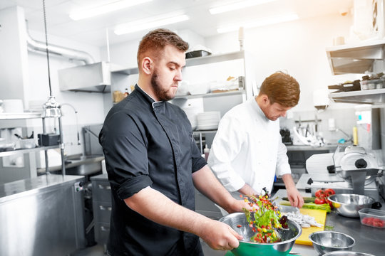 cooking food, profession and people concept - happy male chef and cook with knife chopping champignons and making salad at restaurant kitchen