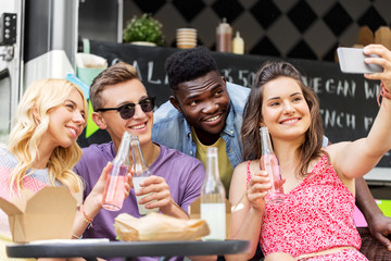 leisure and people concept - happy young friends with food and non alcoholic drinks and taking selfie at food truck